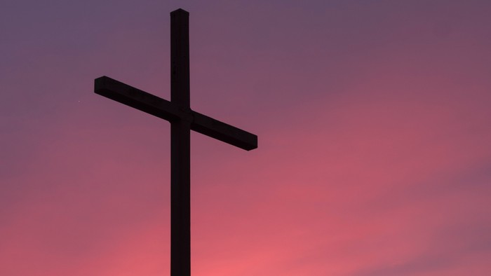 Ein Kreuz vor einem rosa-orangen Himmel