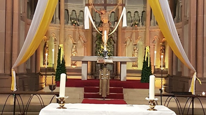 Eleganter Kirchenaltar, geschmückt mit Kerzen, religiösen Symbolen und verziert mit dekorativen Stoffen.