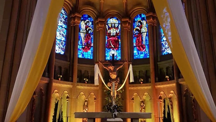 Elegante Kircheninnenausstattung mit Buntglasfenstern, Altar mit Kruzifix und drapierten Altartüchern.