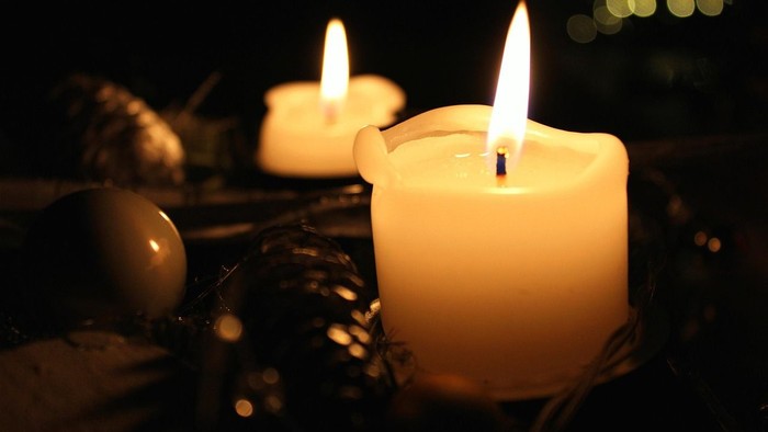 Zwei brennende Kerzen in dunkler Umgebung, eine im Vordergrund mit geschmolzenem Wachsrand.