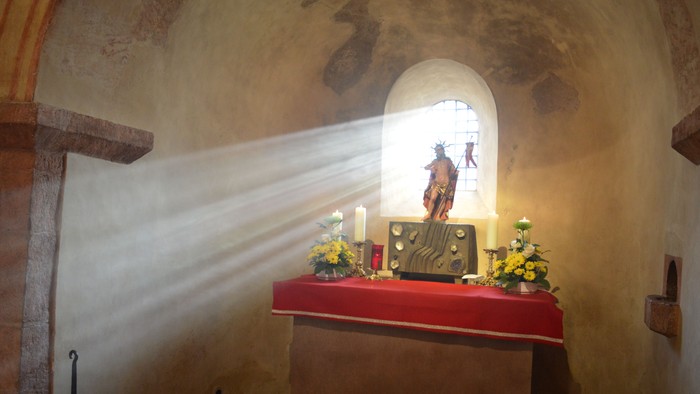 Ein Altar in einer Kirche mit Kerzen und Blumen, beleuchtet durch ein Fenster mit einer Heiligenfigur