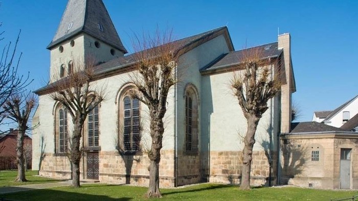 Ein weißer Kirchenbau mit spitzem Turm und großen Fenstern vor blauem Himmel.