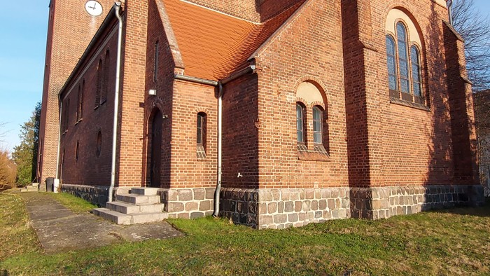 Kirchengebäude aus Ziegeln mit spitzem Turm und mehreren Fenstern