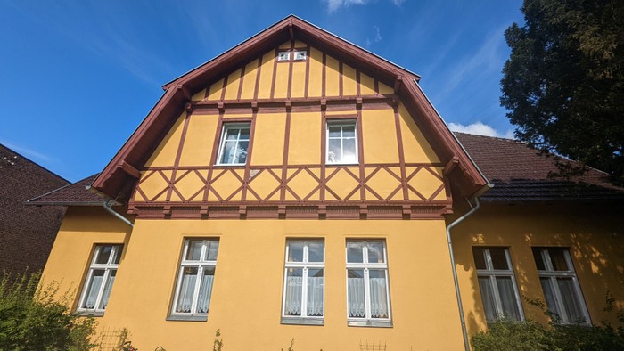 Ein gelbes, zweistöckiges Haus mit braunem Holzfachwerk und weißen Fenstern unter einem klaren blauen Himmel.