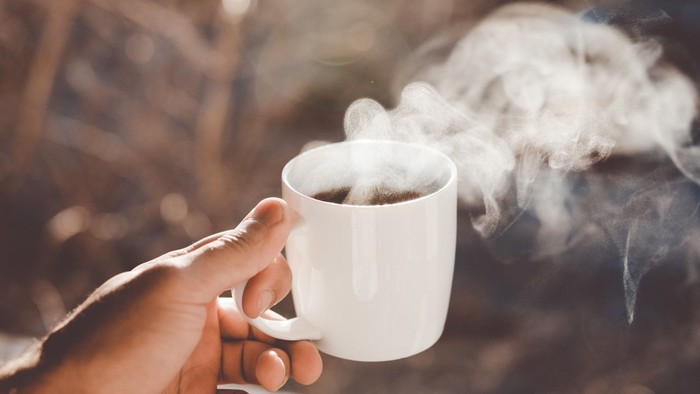 Hand holding a steaming cup of coffee on a wooden railing.
