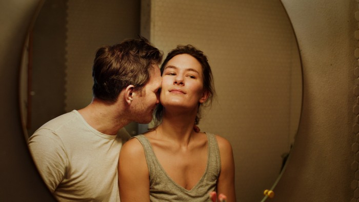 Et par, der deler et intimt kys, mens de kigger ind i et rundt spejl.