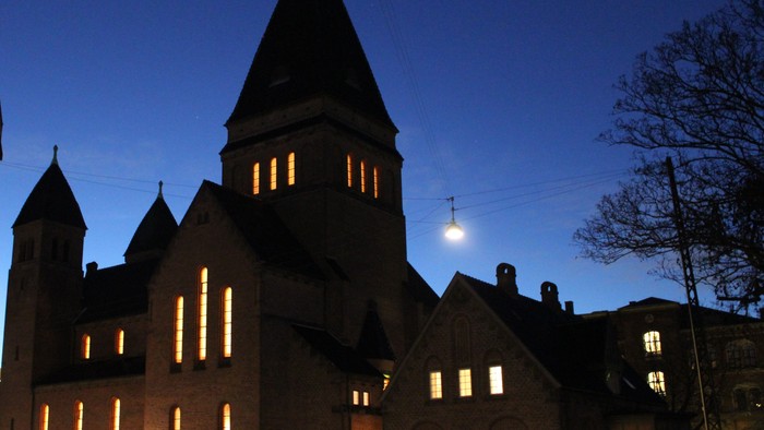 En stor kirke med to tårne og lysende vinduer ved aften.