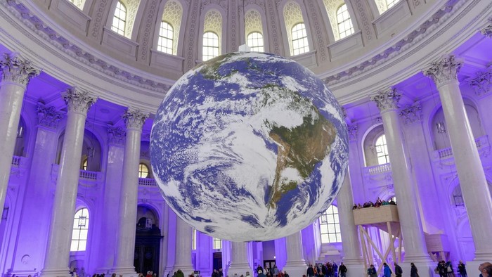 Großer Globus, aufgehängt in einer prächtigen Halle, mit Menschen, die ihn betrachten.