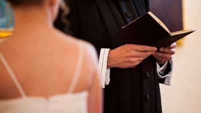 En person i svart kapittel holder en bog og står ved en person i hvid kjole.