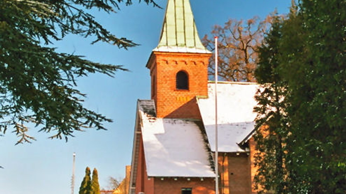 En smuk kirke med tårn og grøn spire, omgivet af sne og træer