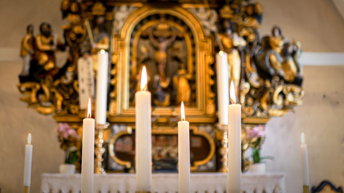 Billedet viser lysede lygter foran en udsmykket altertavle i kirke.