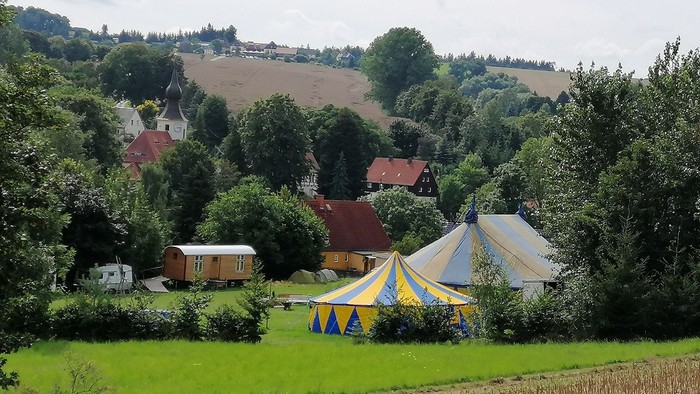 Zelte auf einer Wiese mit Häusern und Bäumen im Hintergrund
