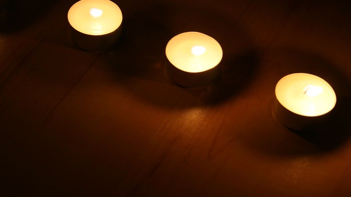 Drei brennende Kerzen in einer Reihe auf dunkler Oberfläche