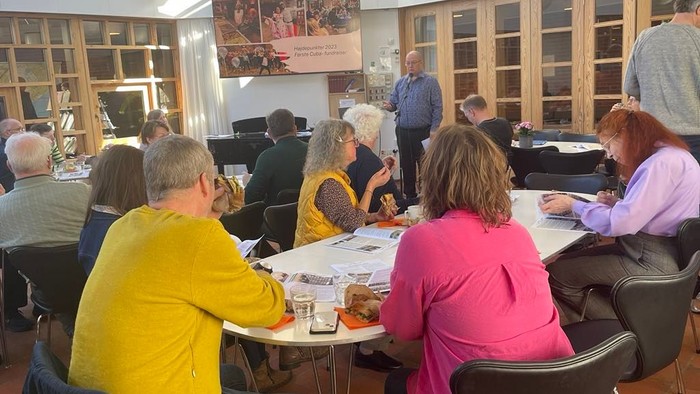 En gruppe af mennesker sidder ved bord i et café og diskuterer.