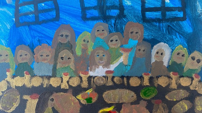 Barn og voksne sidder sammen ved bord med mad