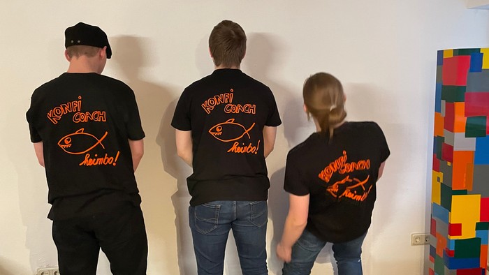 Drei Personen in passenden T-Shirts stehen an einer Wand.