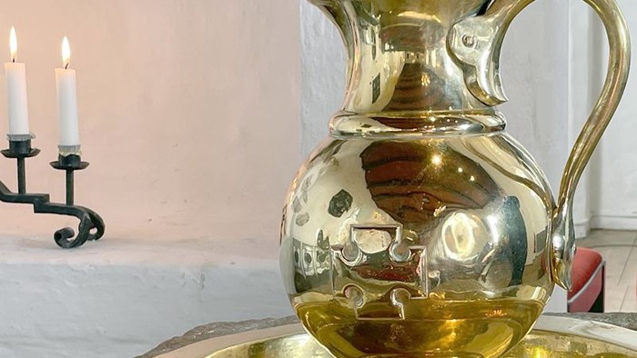 En blank poleret guldfarvet kande står på en marmorsort med to lysede lygter i baggrunden