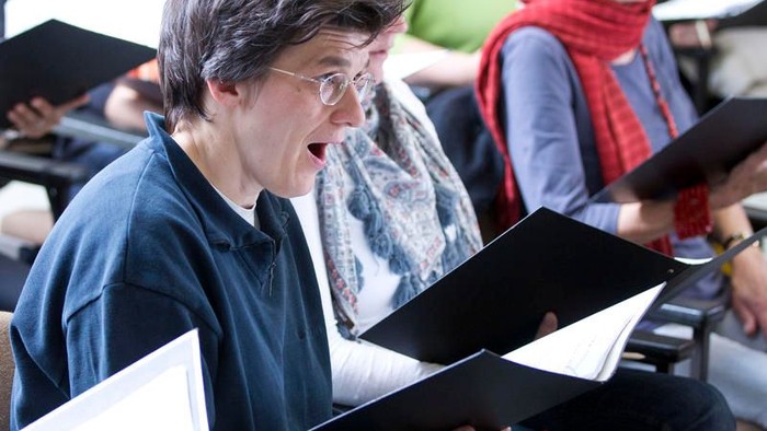 Frau singt in einem Chor und hält Notenheft in den Händen