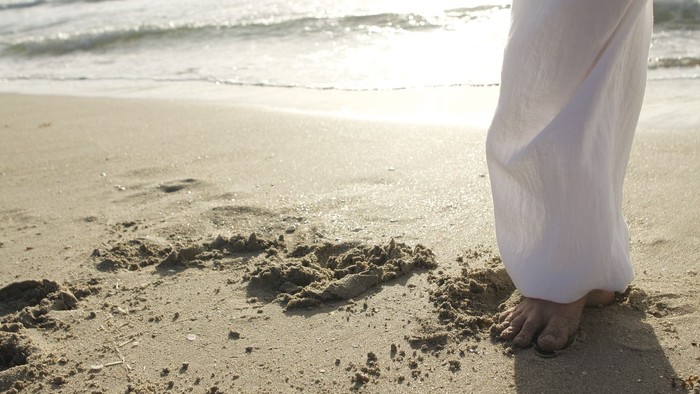 Person steht am sandigen Strand, Fußabdrücke sichtbar