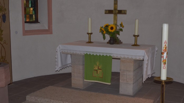 Eine friedvolle Altargestaltung mit einem Kreuz, Kerzen, Blumen und einem grünen Tuch mit einem Kreuzemblem.