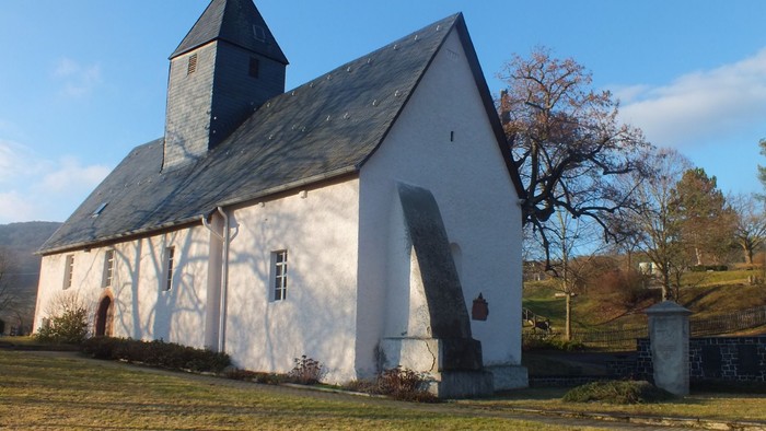 Idyllische weiße Kirche mit steilem Dach und Glockenturm in einer ruhigen, grasbewachsenen Landschaft.