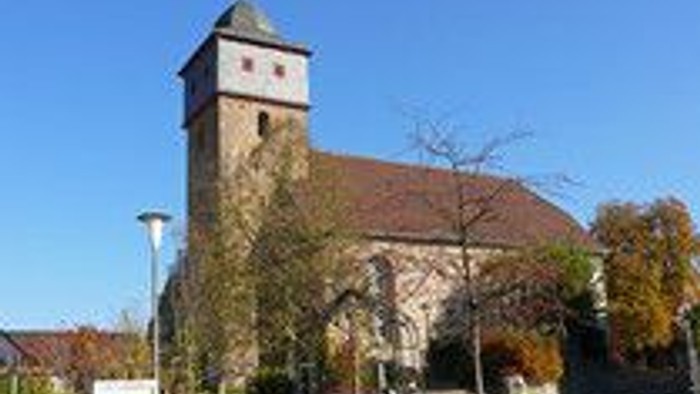 Historische Kirche mit hohem Glockenturm vor klarem blauem Himmel und herbstlichem Laub.