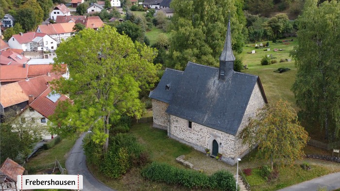 Luftaufnahme einer malerischen Steinkirche in Frebershausen, umgeben von üppigem Grün und Wohnhäusern.