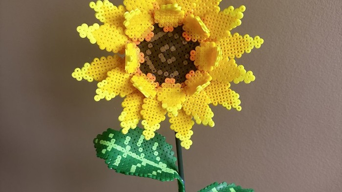 Håndlavet solsikkeudsmykning lavet af farverige perler, der fremviser detaljerede kron- og bladelementer.