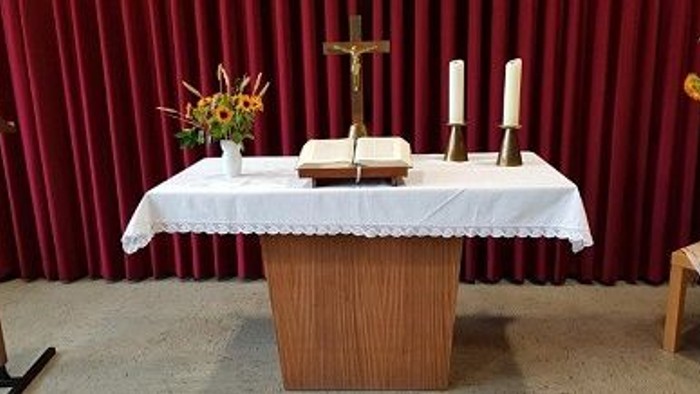 Ein Altar mit weißen Tischtuch, Kerzen und Kreuz vor rotem Vorhang