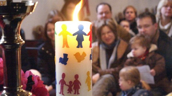 Leute sitzen in Kirche, Kerze mit Kinderbildern brennt