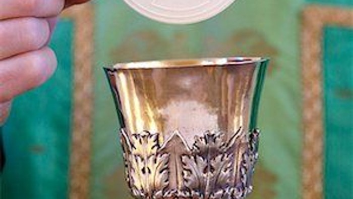 Hand holding wafer above ornate chalice