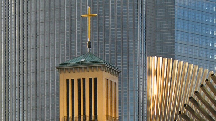 Kirchturm mit goldenem Kreuz vor modernen Hochhäusern