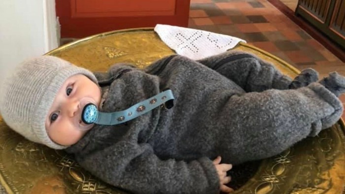 Et børnelev i graa klæder og hvid trøje ligger i en guld skål i kirke.