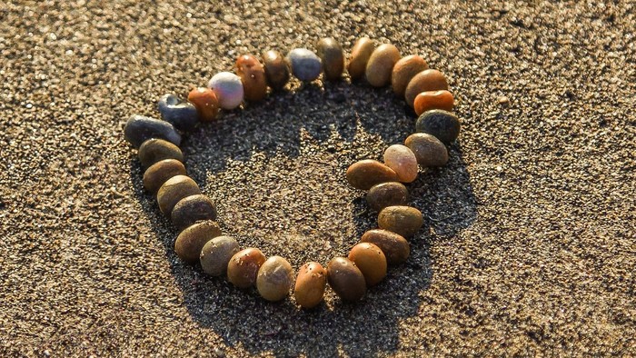 Ein Armband aus Perlen liegt auf sandigem Boden.