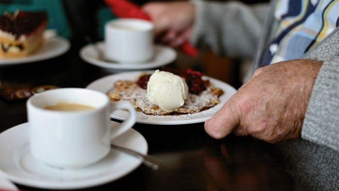 Eine Person hält einen Teller mit Kuchen und Eiscreme, daneben steht eine Tasse Kaffee.