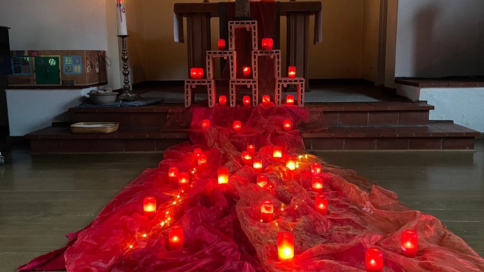 Ein Altar mit einem großen Holzkreuz und vielen roten Kerzen, umgeben von rotem Tüll.