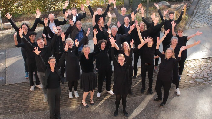 Eine vielfältige Gruppe von Menschen in schwarzer Kleidung hebt fröhlich die Arme im Freien in einer feierlichen Pose.