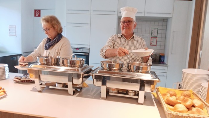 Zwei Personen bedienen sich an einem Buffet in einer Küche.