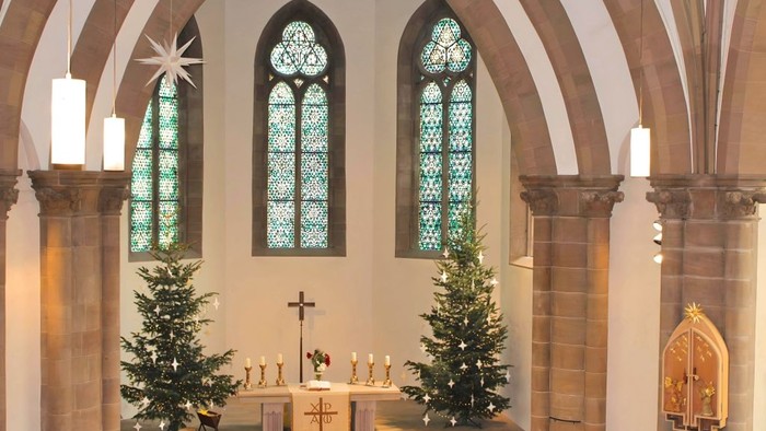 Elegantes Kircheninneres mit geschmückten Weihnachtsbäumen, Buntglasfenstern und einem friedvollen Altaraufbau.