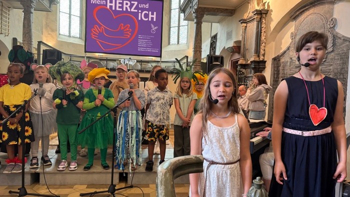 Kinder singen in einer Kirche mit einem Banner hinter ihnen.