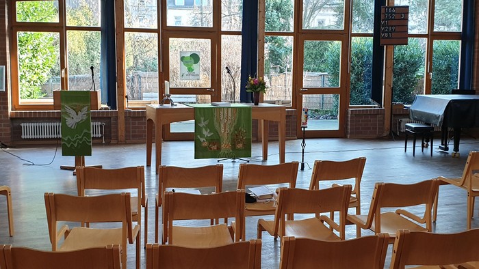 Ein Raum mit Holzboden, Stühlen und großen Fenstern, die auf einen Garten hinausgehen.