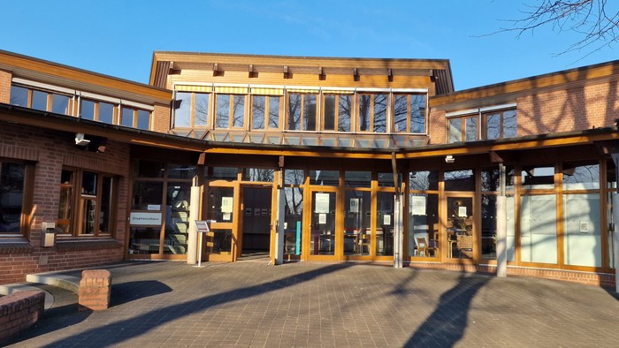 Das Bild zeigt ein modernes Gebäude mit großen Fenstern und einem überdachten Eingangsbereich.