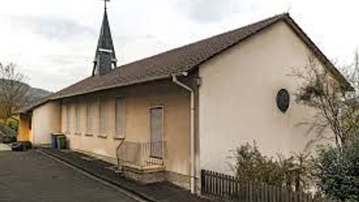 Kleine Kirche mit spitzem Turm und Holzbank davor.