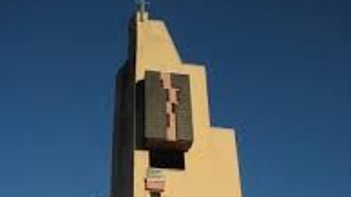 Das Bild zeigt eine moderne Kirche mit einem großen Kreuz vor einem klaren blauen Himmel.