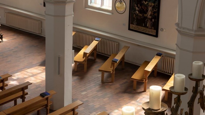 Seitenschiff einer Kirche mit hölzernen Kirchenbänken und hohen, weißen Säulen.