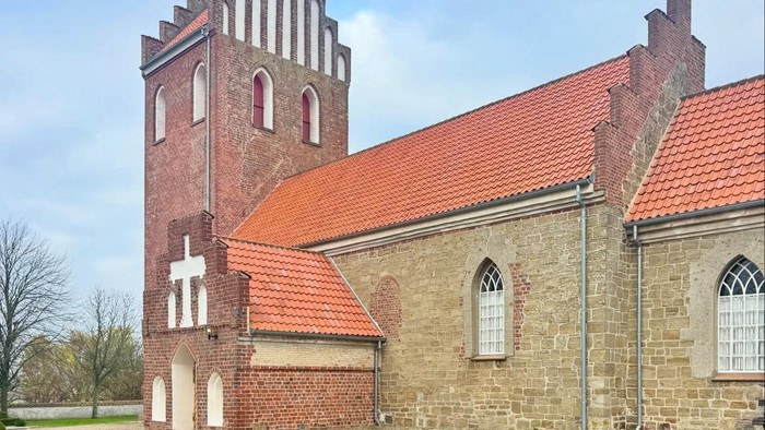 Historisk stenkirke med rødt tag og højt tårn.