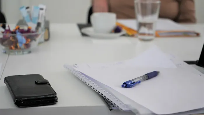 En skrivebord med notebog, pen, mobiltelefon og en kop kaffe.