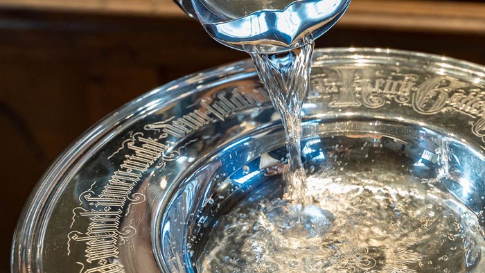 Wasser wird aus einem silbernen Krug in eine Glas-Schale gegossen