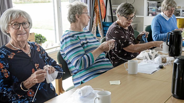 En gruppe pensionister sidder ved bord og laver håndarbejde.