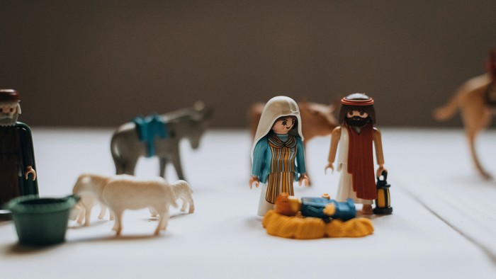 Playmobilfiguren, Maria und Josef, Jesuskind vor ihnen, im Hintergrund unscharf Tiere